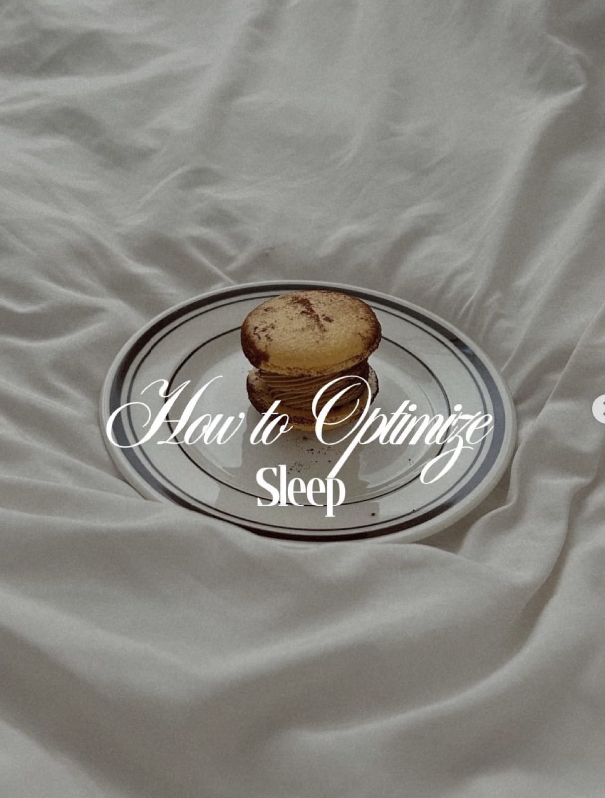 A single macaron on a small plate, set on rumpled white bed sheets